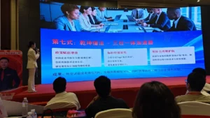 Presenter speaking to an audience beside a blue business presentation screen